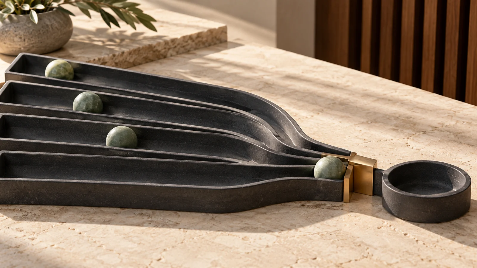 Graphite channels holding green spheres converge towards a narrow brass outlet beside a dark round bowl